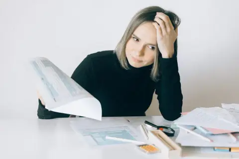 Kobieta zamyślona nad dokumentami, z ręką na czole, przy biurku ze stertą papierów.